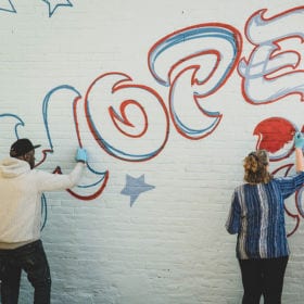 At the Friends of the Homeless Shelter, artist Wane One (at left) left paints the mural “Hope is Welcome Here” with shelter guests.